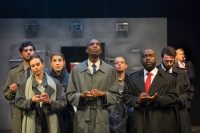 Group of actors on stage all wearing raincoats and pretending to write