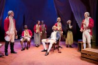 Actors sat and stood on stage dressed in old fashionned uniform