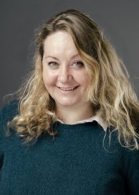 Headshot of woman with long blonde curly hair in a dark teal top