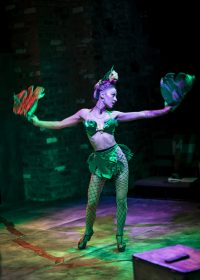 Actress stood with arms outstretched wearing a bikini top, and lace tights with leaf adornment