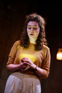 Female actor on stage with hands together, looking down