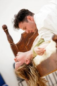 Female actor lying on bed with eyes closed, male actor on top