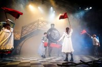 Female to the left, facing front, waving a red flat, female in the middle with her back showing, waving a red flag, male to the right facing side on waving a red flag, female actor and two males in middle holding front model of a steam train