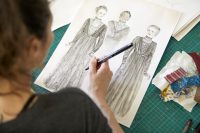 Close up of student holding pen and a drawing of costumes