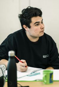 Student sat at desk, holding pencil with open book