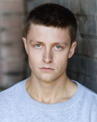 Headshot of man with short brown hair looking directly at camera with a serious expression