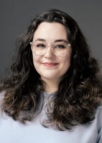 Headshot of smiling woman with dark brown hair glasses and a blue top