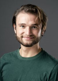 Headshot of smiling man with short brown hair and a beard in a green top