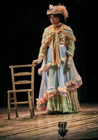 Actress posing by chair in ornate gown and hat