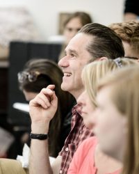 Close up of male in middle of photograph surrounded by others (out of focus)