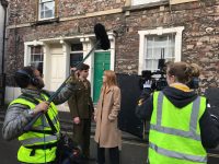 Image of actors and crew in the street wearing hi viz and stood around a camera