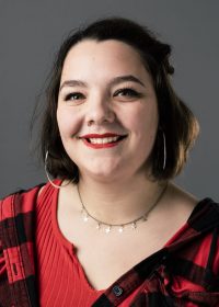 Headshot of a female smiling at the camera with dark hair in a bob wearing a red and black top