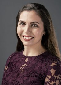 Headshot of smiling woman with long brown hair and a purple lacey top