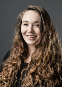 Headshot of woman smiling at camera with long brown curly hair