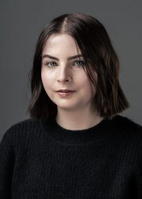 Headshot of female student with short black bob length hair looking at the camera, wearing a black long sleeve top