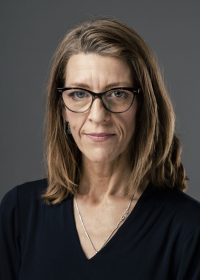 Headshot of woman with light brown hair and glasses wearing a black top