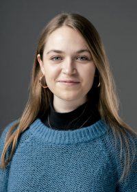 Headshot of woman with long dark blonde hair, hoop earrings and a blue jumper