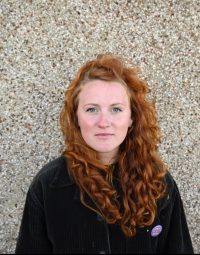 Woman with long red hair stood looking directly at the camera