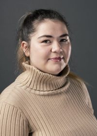 Headshot of woman in a brown top with brown hair in a ponytail