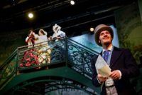 Three actors stood high up on a bridge and another actor stood down below, all in Edwardian costume