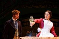 Two actors on stage, one pouring liquid into a pot, both in Edwardian costume