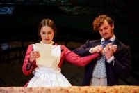 Two actors on stage, one reading from paper, the other holding onto her other hand