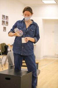 Actor stood pouring from a bottle into a mug