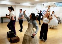 Actors in rehearsals, one stood on a box, another holding a parasol, another holding a megaphone