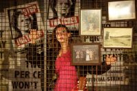 Actor stood on stage behind wired wall covered with old photos