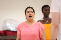 A woman wearing a pink shirt sings in a rehearsal studio